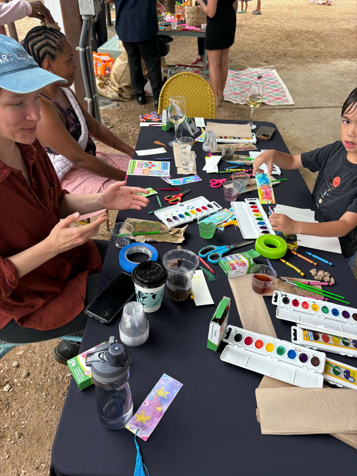 People gathered around a table with art supplies, including watercolors, brushes, and paper, engaging in a creative activity.