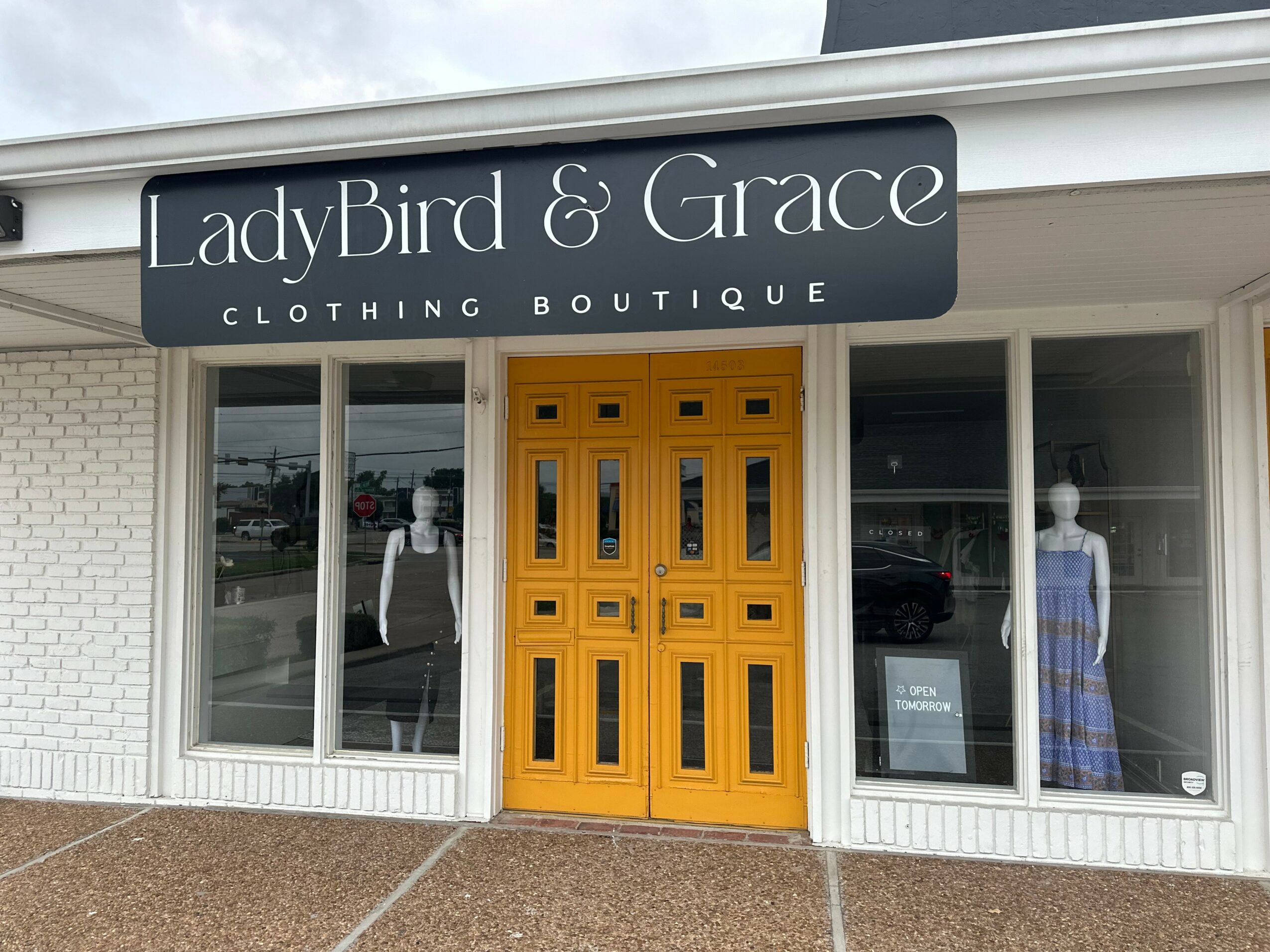 Clothing boutique storefront with yellow door, large windows, and mannequins inside, sign reads 'LadyBird & Grace'.