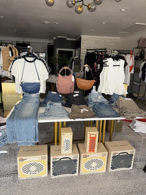 Clothing display with jeans, shirts, and handbags in a store, with boxes on the floor, ceiling lights, and racks in background.