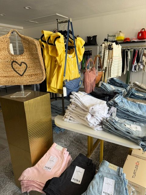 Clothing store with folded clothes, hanging garments, and a yellow raincoat on a rack, viewed from the side.