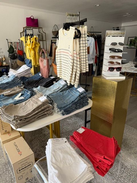 Clothing store with racks of clothes, folded jeans on table, and boxes on the floor.