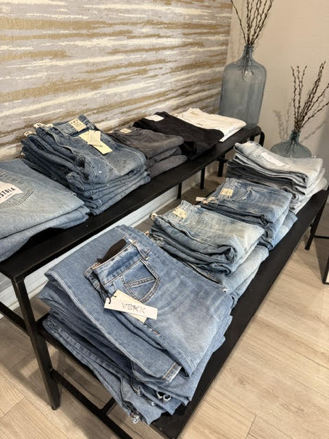 Tables display folded jeans in various shades of blue and black, with vases and decorative branches in the background.