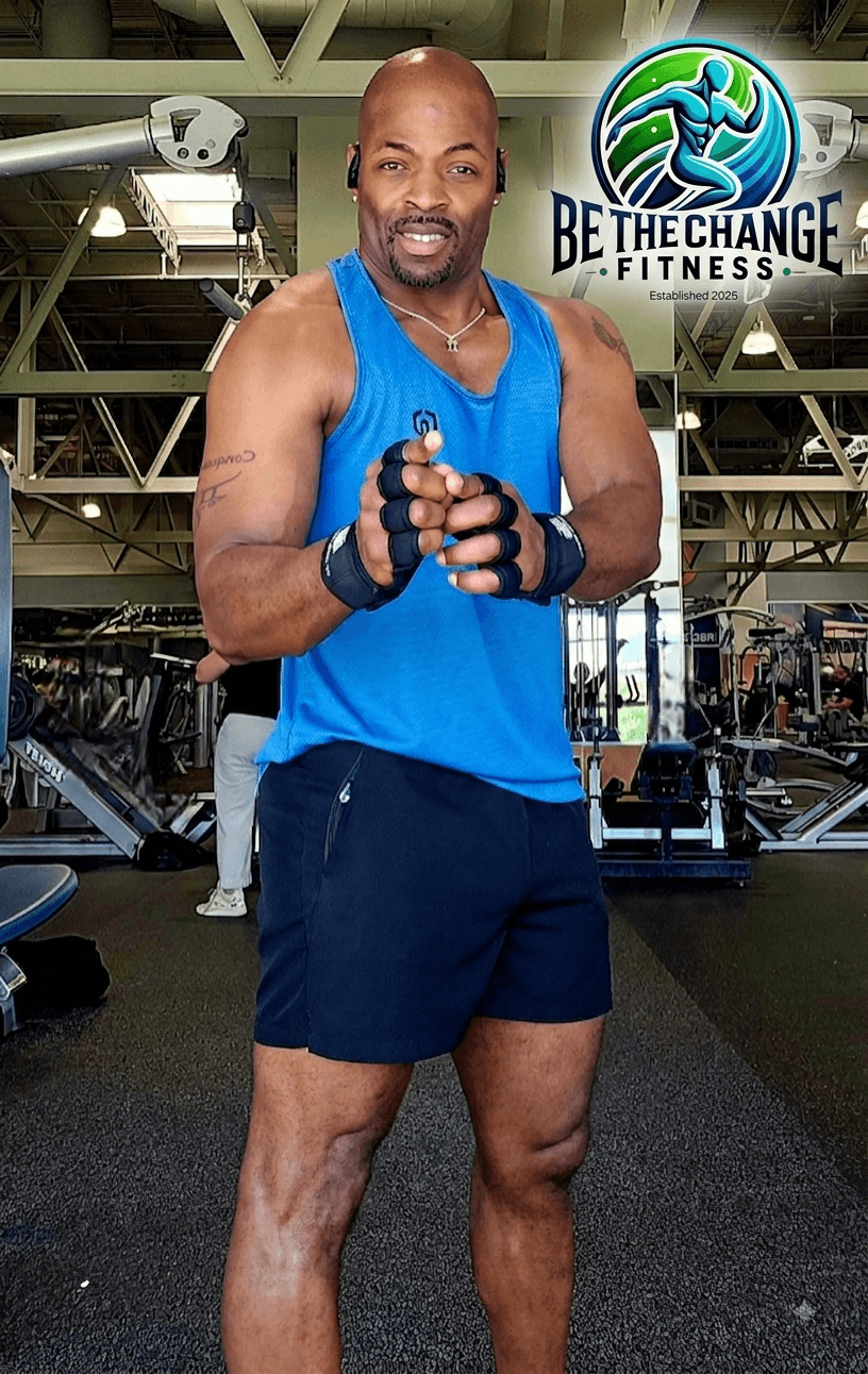 Man in blue workout shirt and shorts standing in gym, smiling, with fitness logo in background.