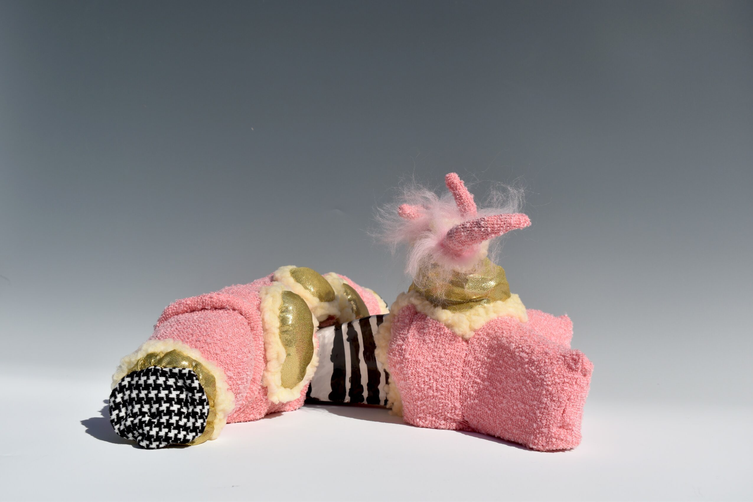 Pair of plush slippers with pink, black, and beige colors, one with a fluffy pink bow, on a gray background.