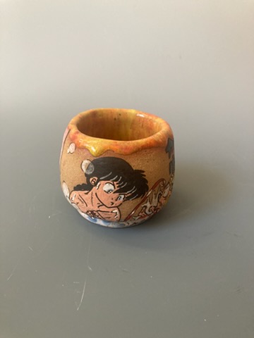 Small ceramic pot with a painted cartoon character, placed on a gray surface against a plain background.
