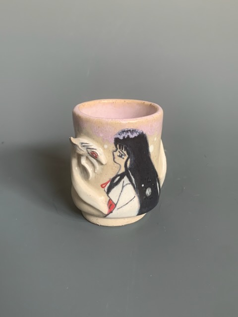 Ceramic cup with a painted dragon and a woman with long black hair, pink dress, against a plain background.