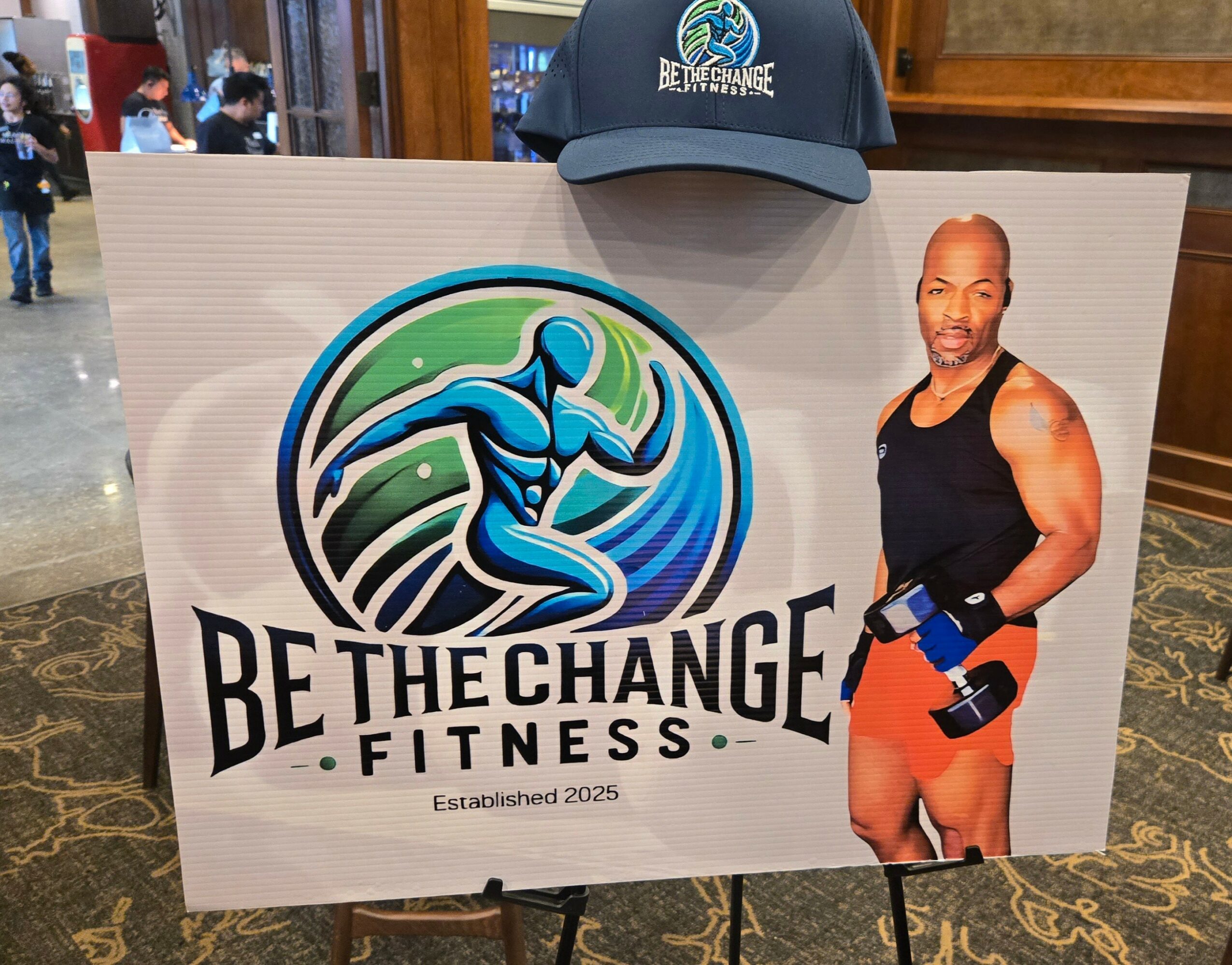 Fitness promotional sign with a blue running figure, a man in workout attire, and a cap on top, promoting fitness.