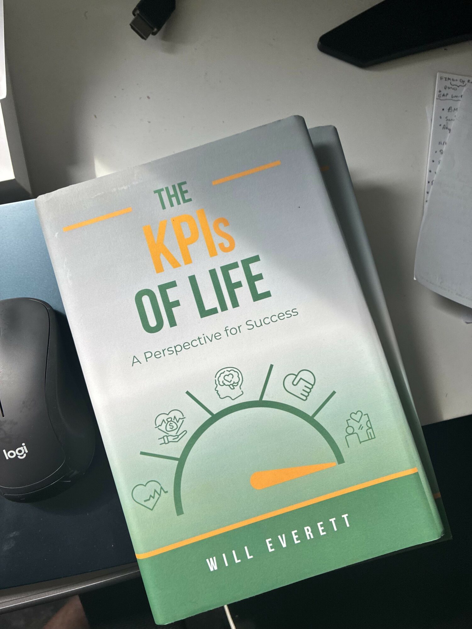 Book titled 'The KPIs of Life' by Will Everett on a desk, with a black mouse and paper nearby.
