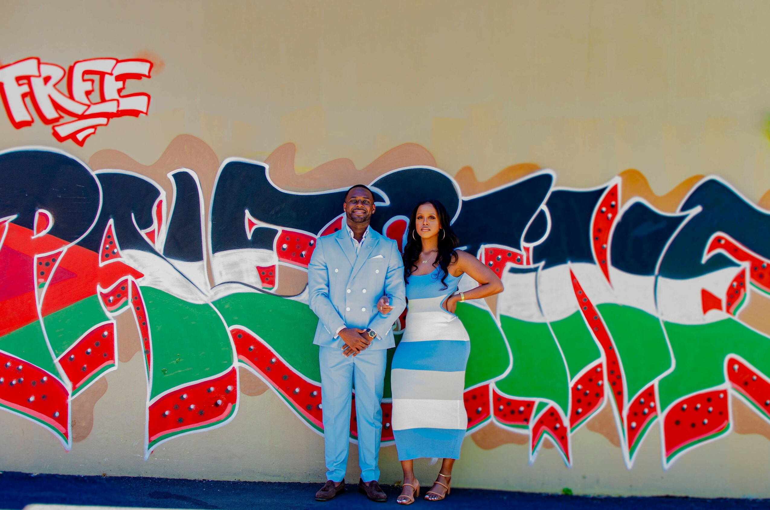 Two people stand in front of a colorful graffiti wall with red, green, and blue designs.
