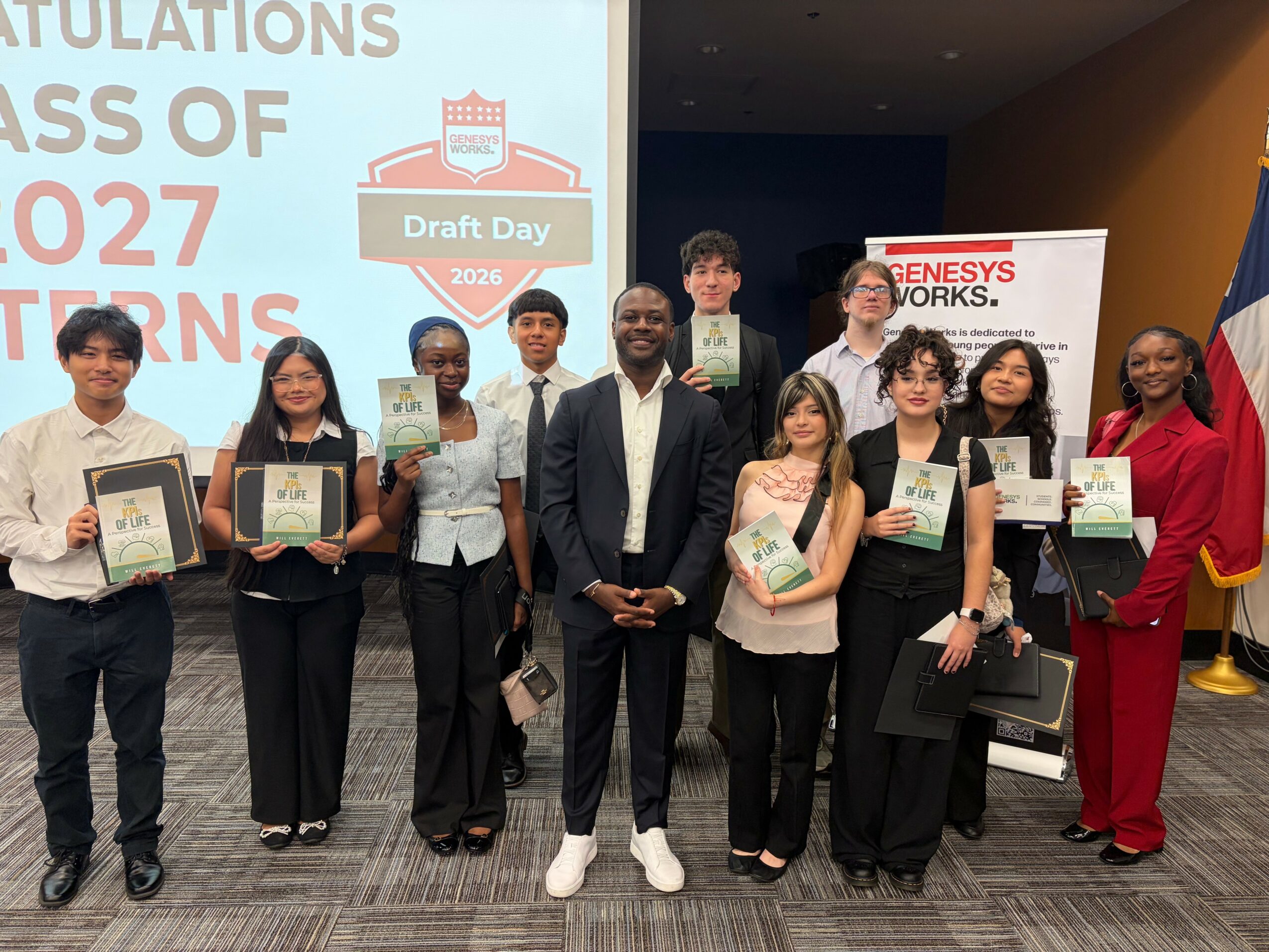 Group of ten people standing indoors, holding certificates or awards, with a large screen and banners in the background.