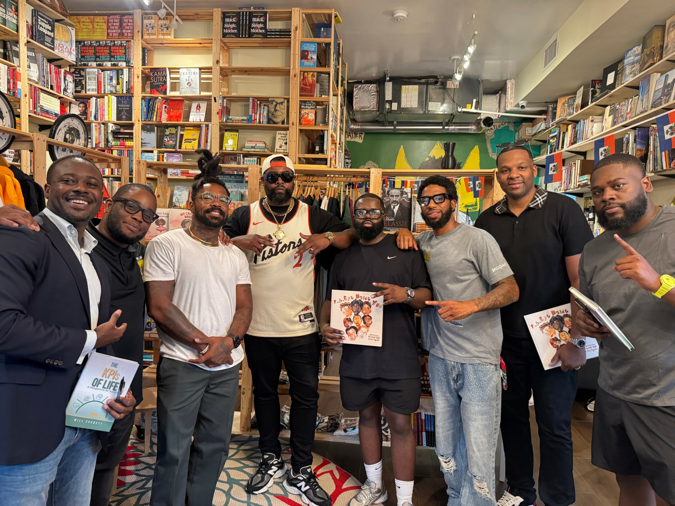 Group of nine people standing in a bookstore, some holding books, smiling, with shelves filled with books behind them.