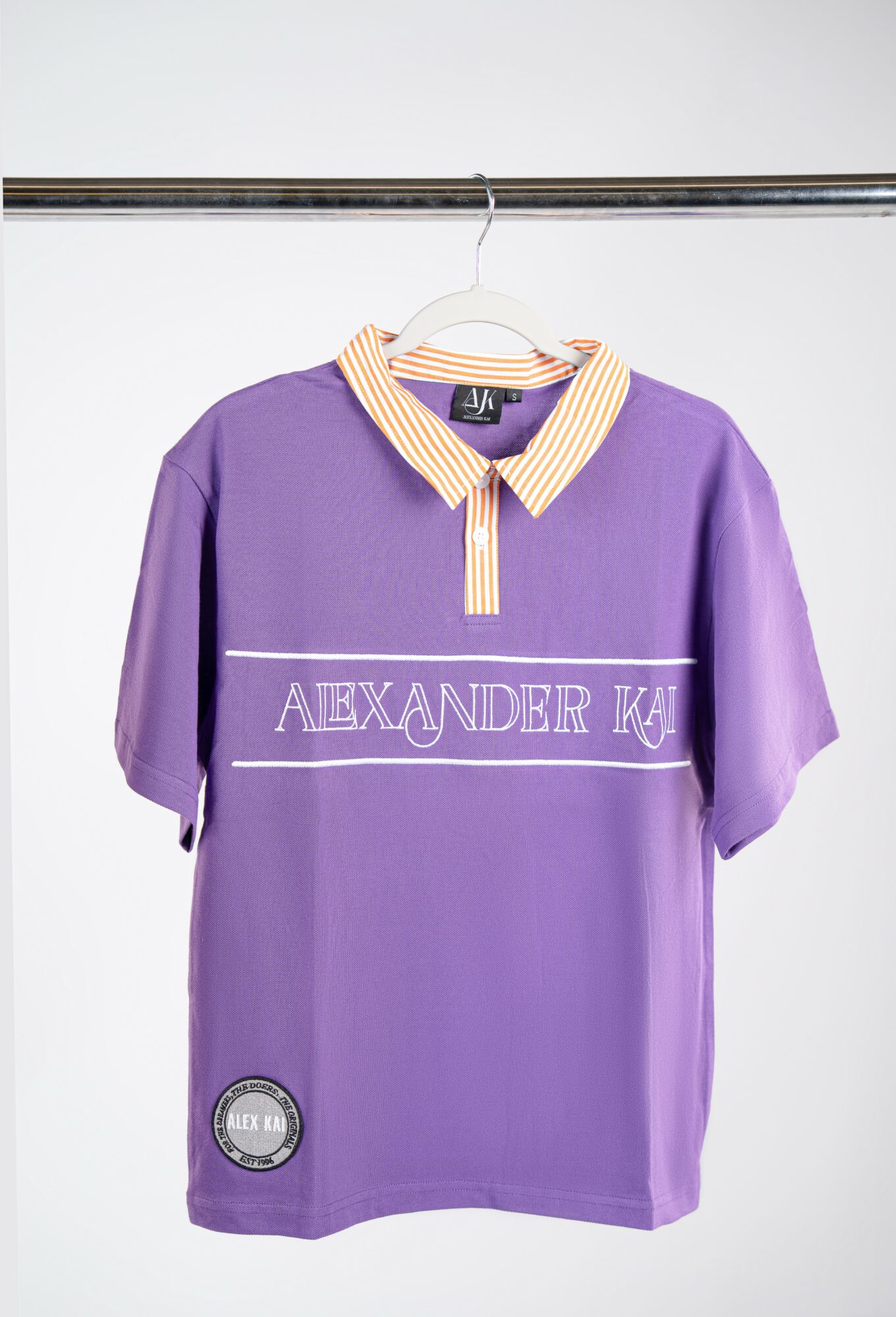 Purple short-sleeve shirt with a yellow and white striped collar hanging on a hanger against a white background.