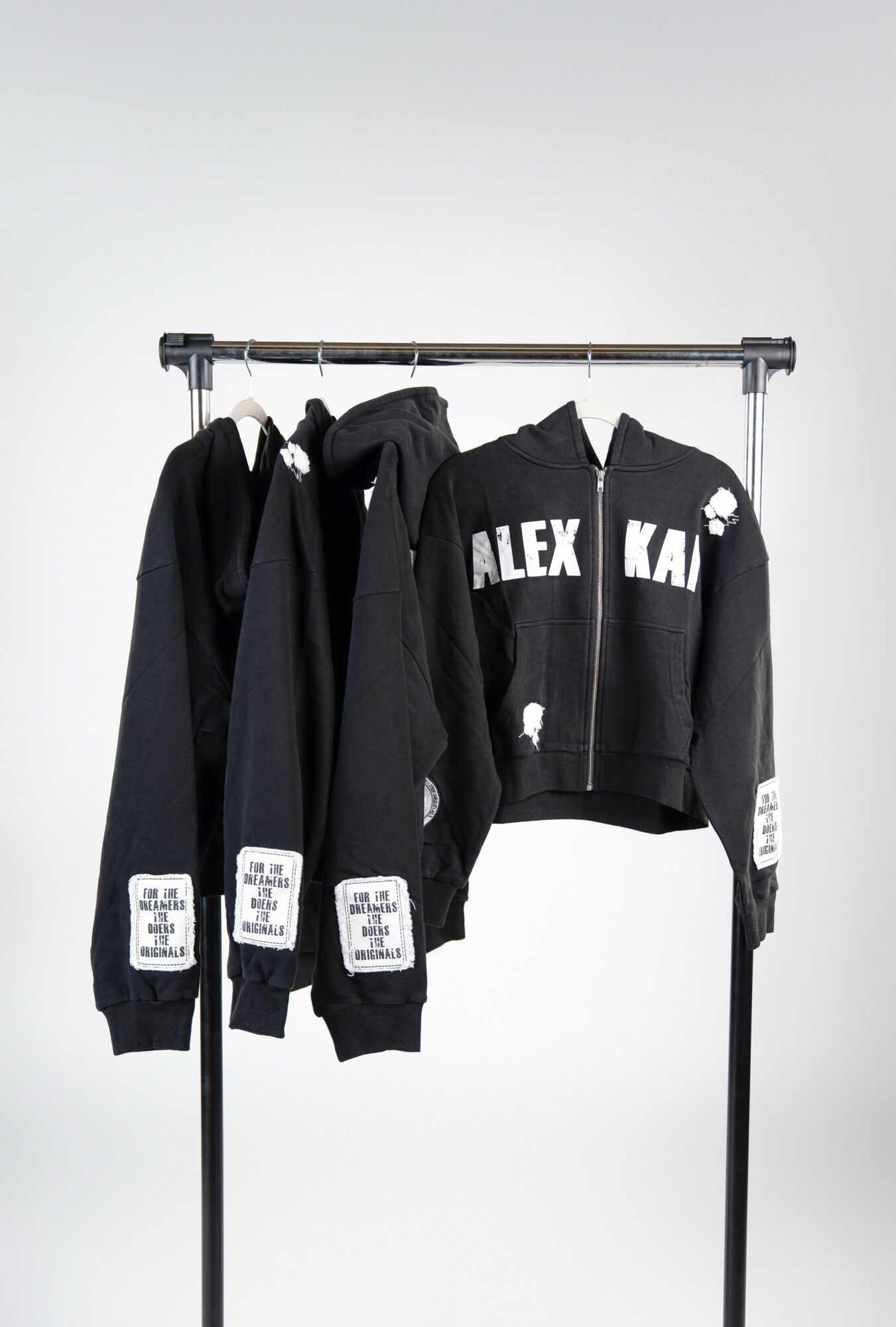 Three black jackets hanging on a metal clothing rack against a plain background.