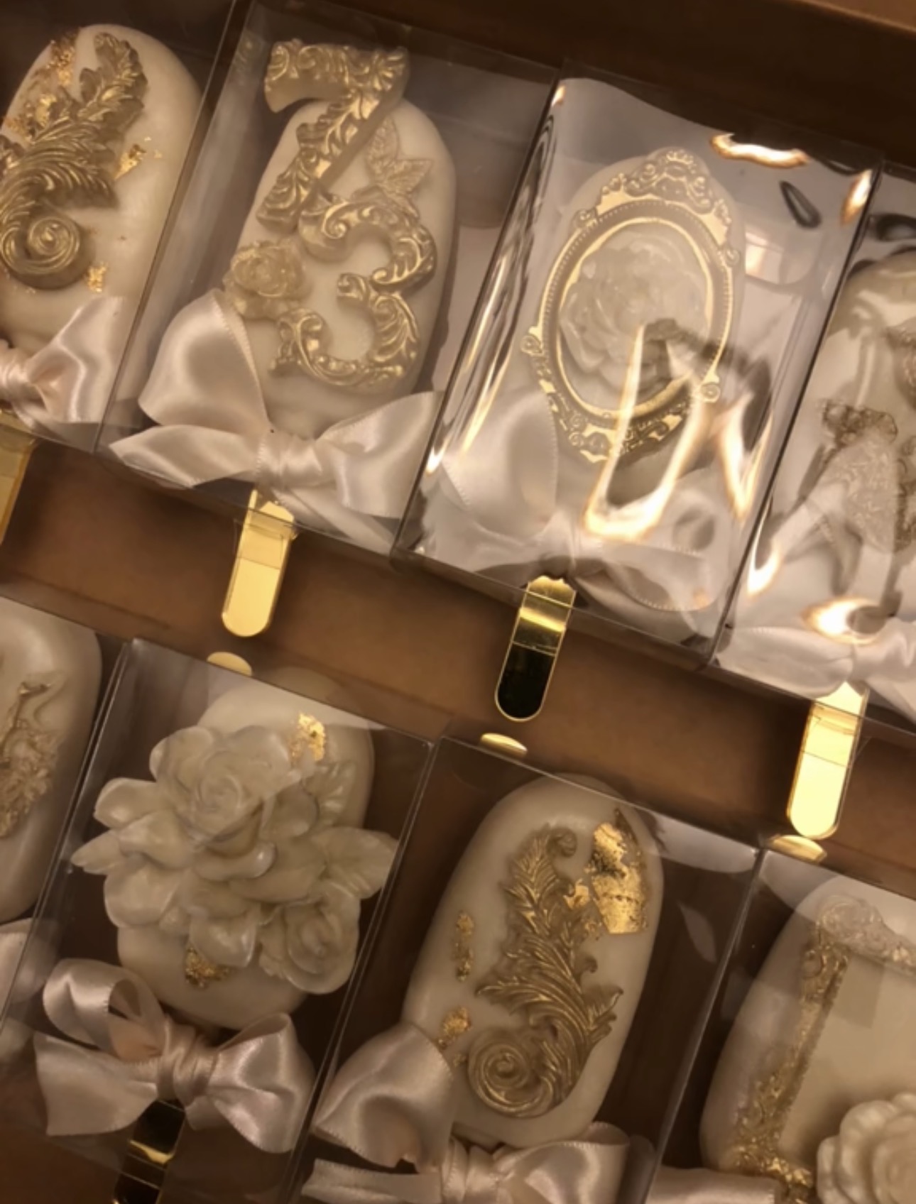 Decorative candles with gold and white designs, some with bows, arranged in a box.
