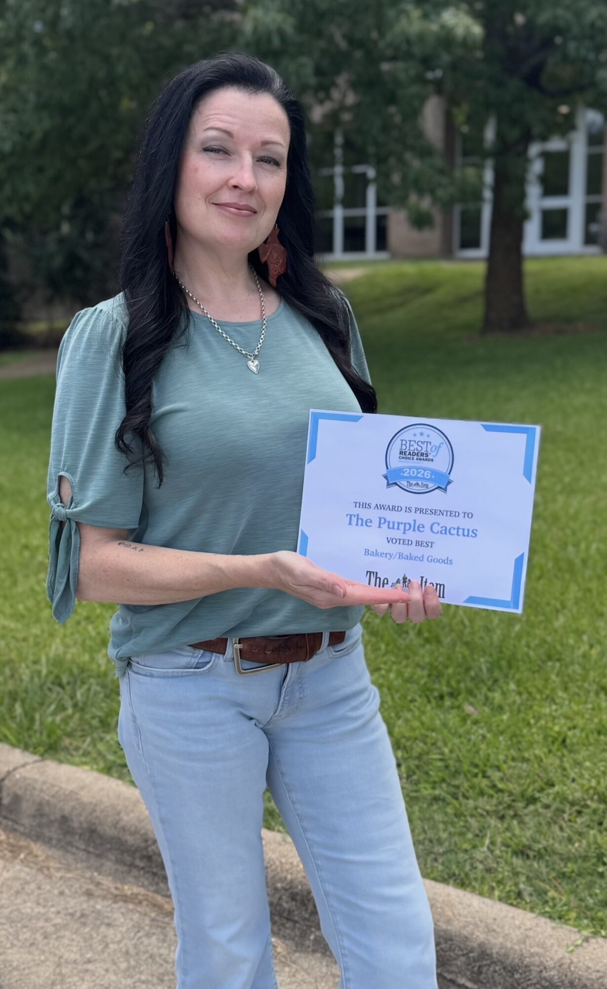 Woman holding a certificate outdoors with trees and a building in the background.