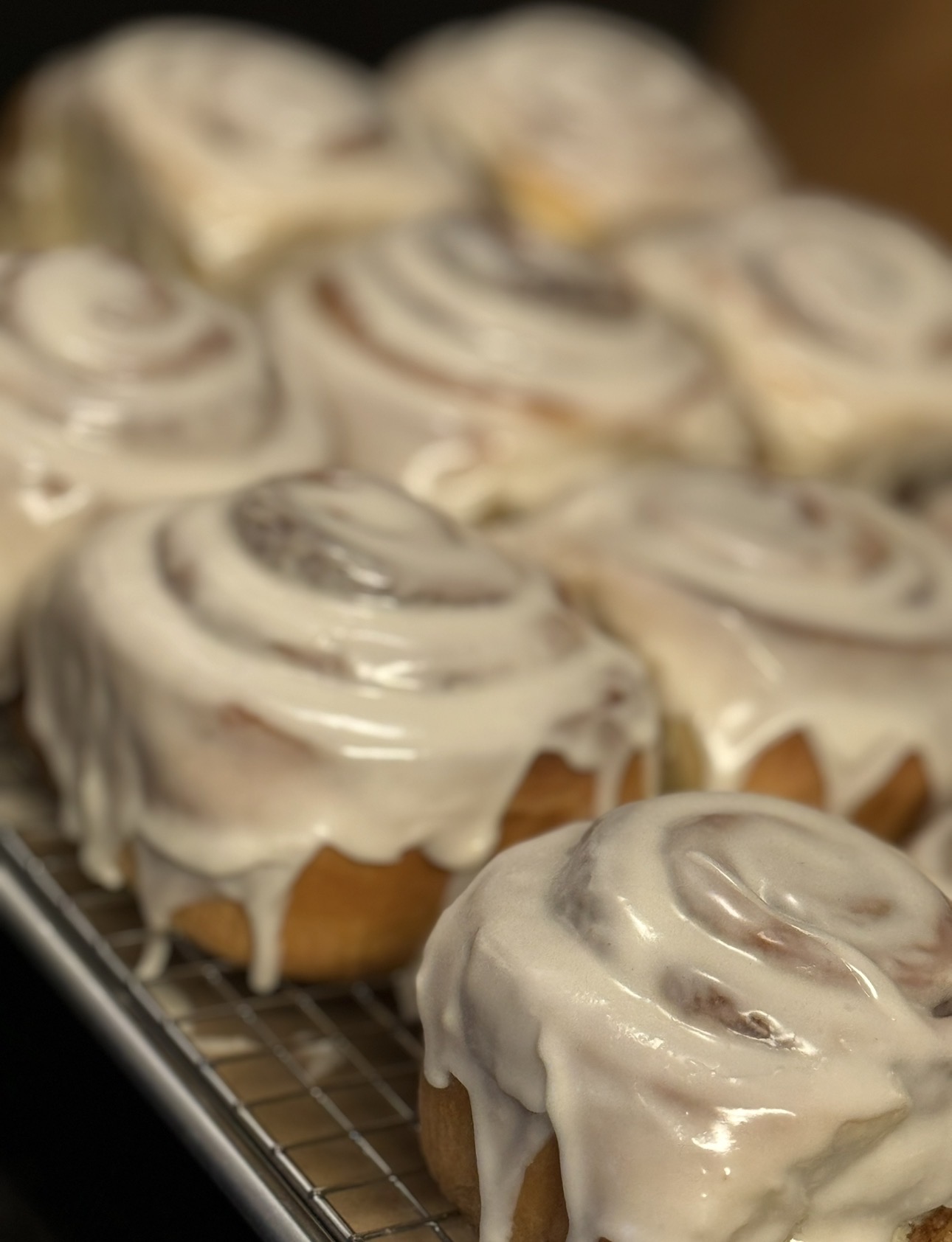Several cinnamon rolls with white icing on a wire rack, some with visible swirls of cinnamon filling.