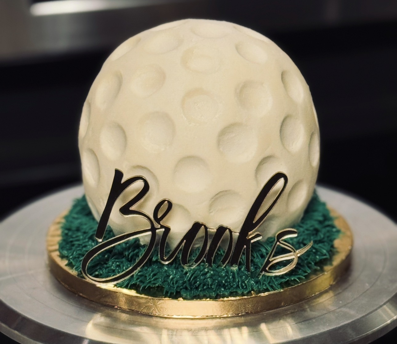 Cake with a moon-like sphere, green grass decoration, and a black cursive 'Bunk' sign, on a round base.
