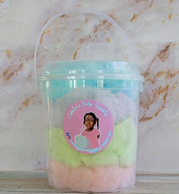 Clear plastic bucket with a handle, containing colorful cotton candy, sticker with a girl, pink, green, and blue colors, on a marble surface