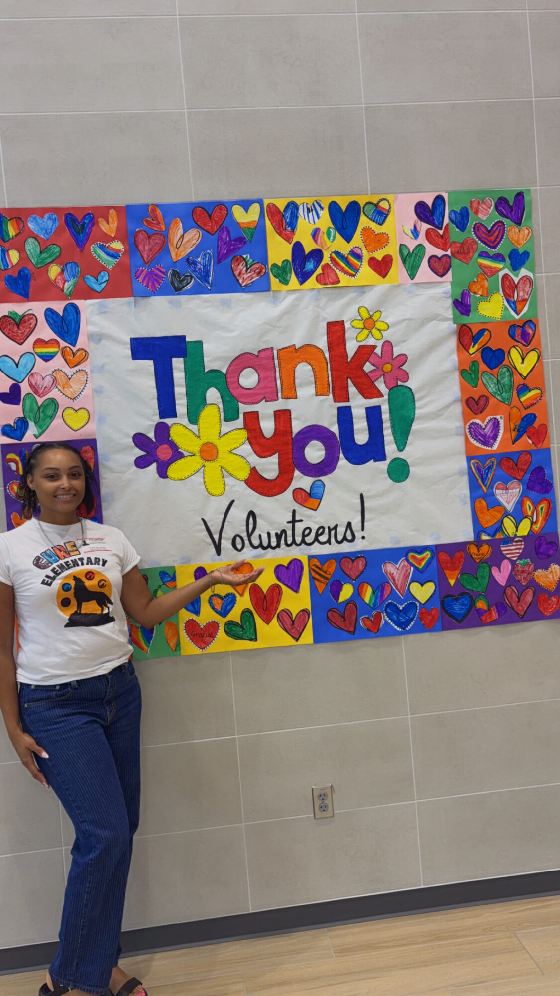 Girl standing next to a colorful thank you poster with hearts and flowers on a tiled wall.