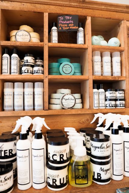 Wooden shelf with skincare products, bottles, jars, and a small chalkboard sign, with spray bottles and a soap dispenser in front.