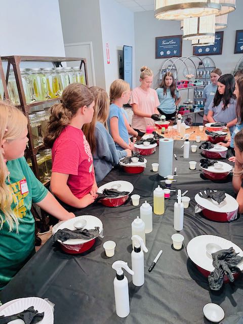 Children gather around a table with black tablecloths, preparing for a cooking activity in a classroom setting.