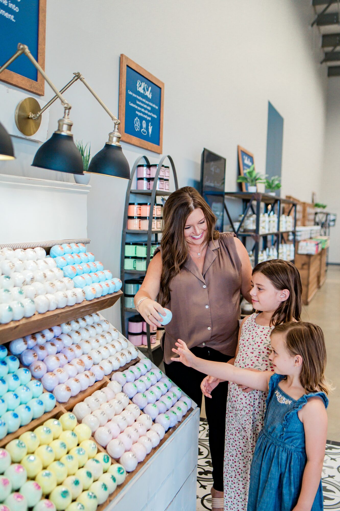 Woman and two children shopping for eggs in a store with shelves and colorful eggs displayed.