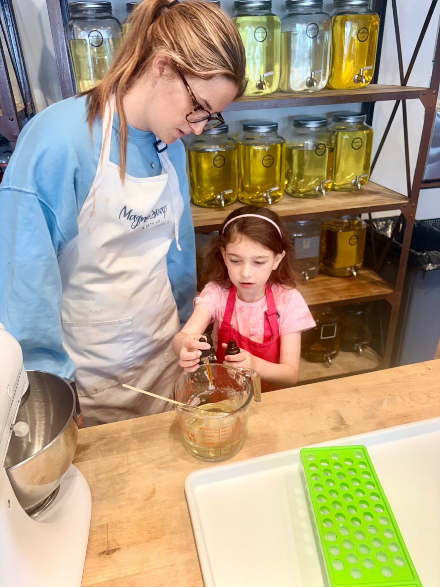 Adult and child mixing ingredients in a glass bowl in a kitchen or workshop setting.