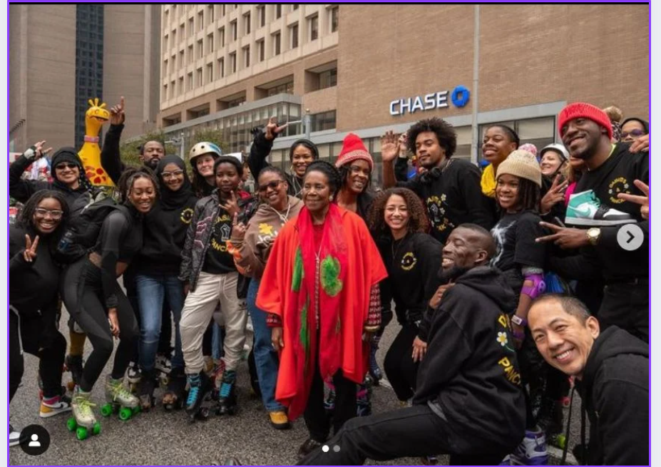 Group of people outdoors, some wearing colorful clothing, smiling, and posing for a photo in front of a building with a Chase sign.