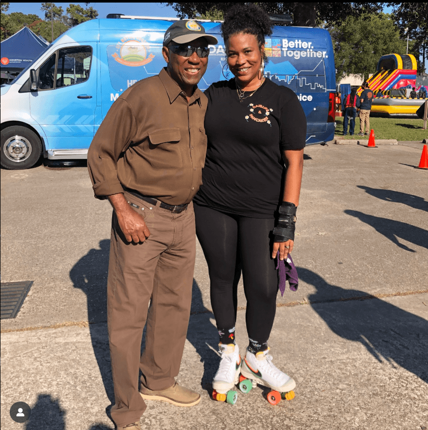 Two people, one in roller skates, standing outdoors with a blue van and inflatable bounce house in background.