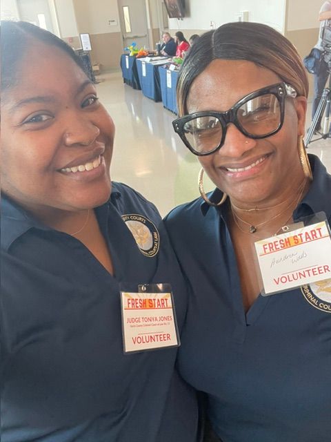 Two women wearing volunteer badges and navy uniforms smiling indoors.