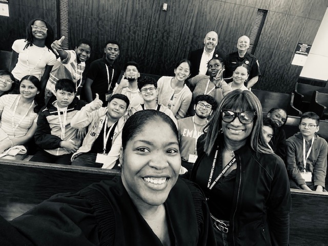 Group of diverse people in a room, smiling and posing for a photo, with two women in the front.