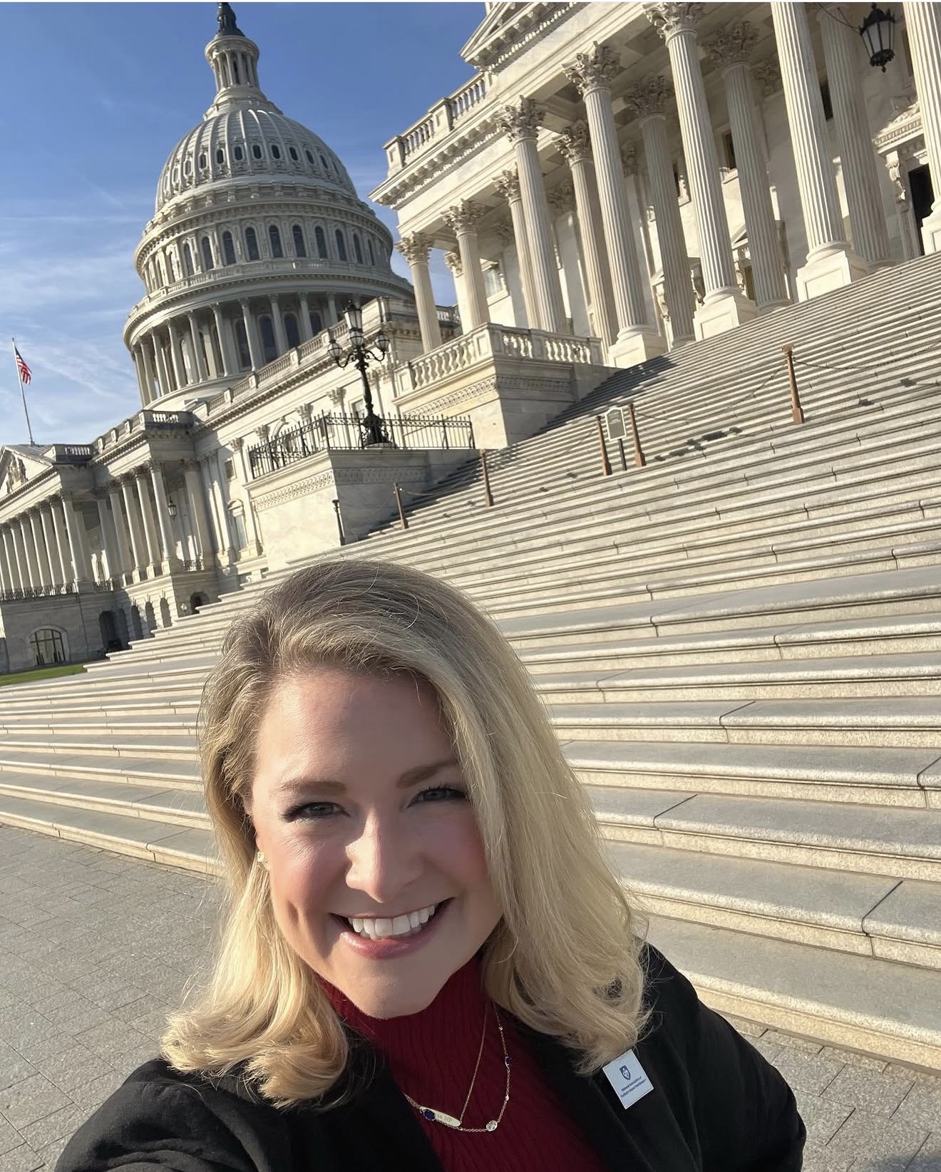 Woman with blonde hair smiling in front of the U.S. Capitol building with stairs and columns.