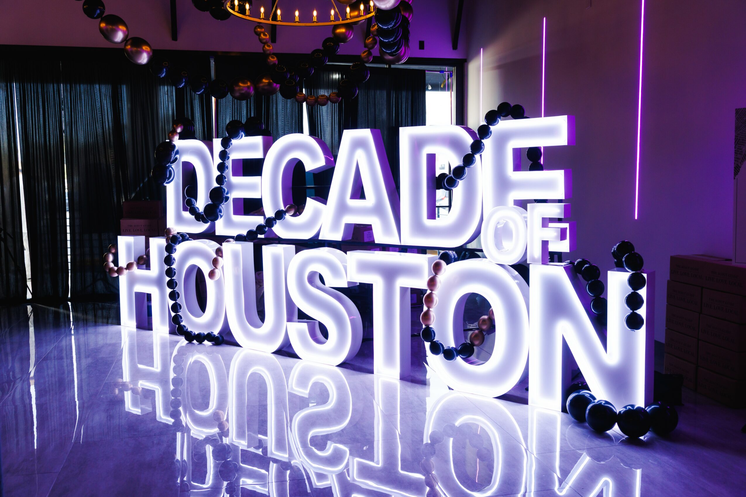 Illuminated sign reads 'Decade of Houston' in a room with purple lighting and black decorations.
