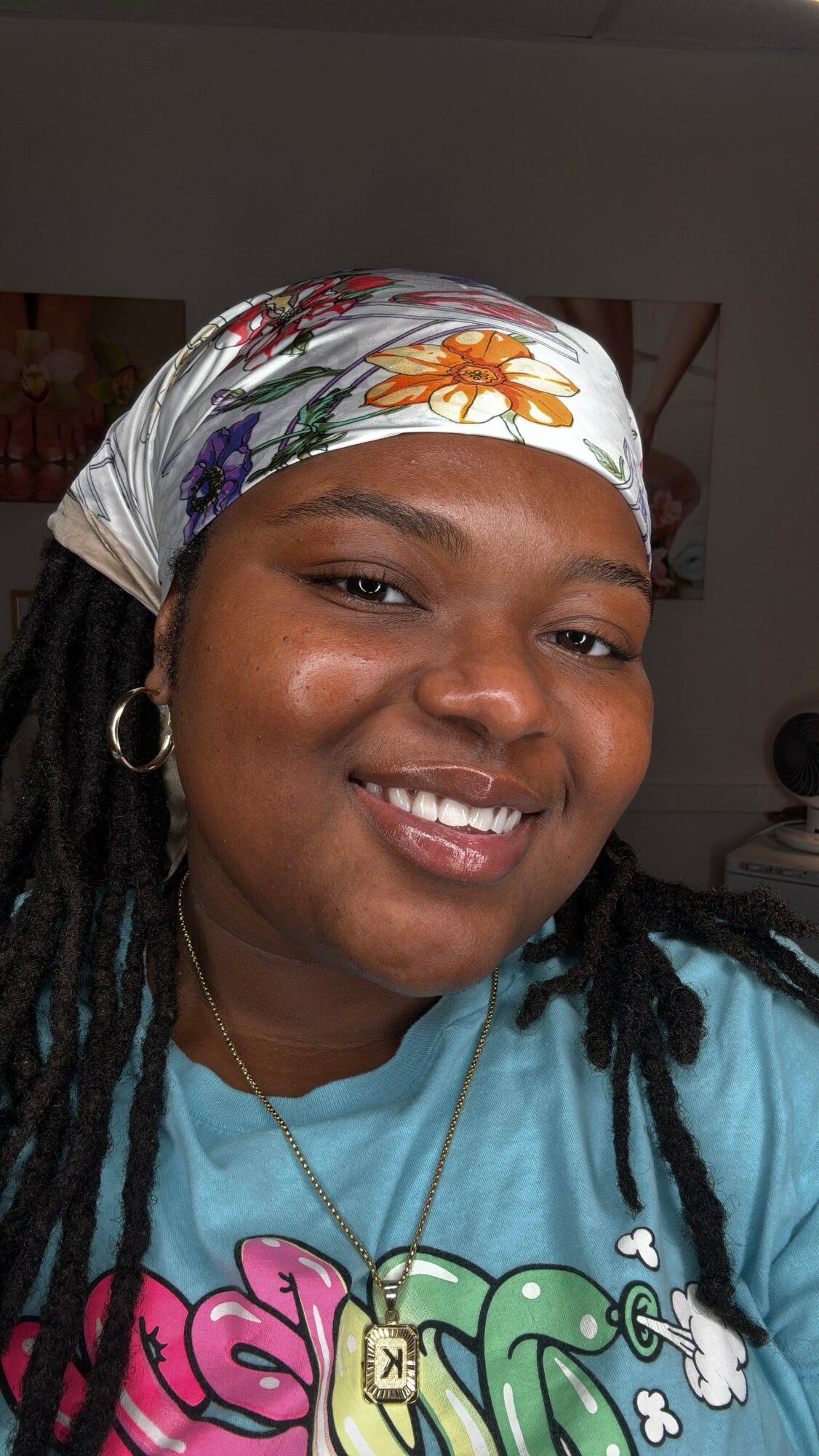 Smiling woman wearing a colorful headscarf and a blue shirt with pink and green text, indoors.