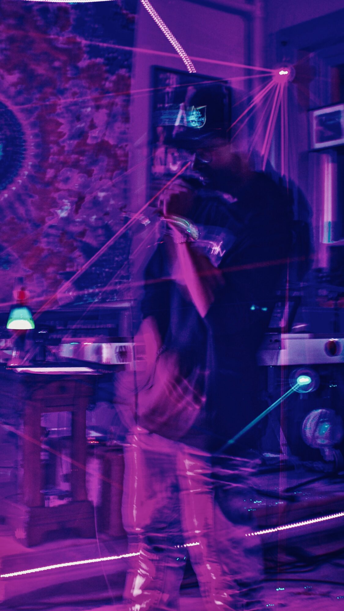 Person in a room with colorful lights and a tapestry, taking a mirror selfie with a phone, surrounded by neon effects.