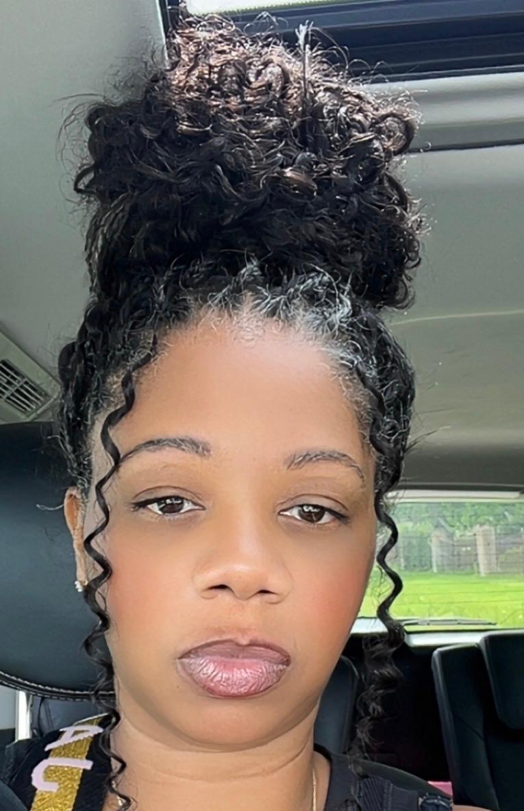 Woman with curly hair styled in a high bun, sitting in a vehicle, looking at the camera.