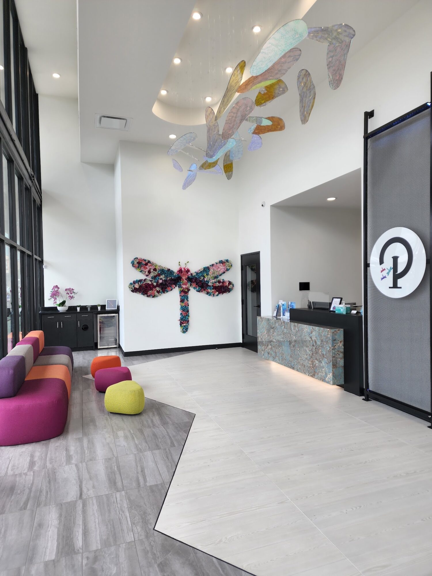 Lobby with colorful seating, dragonfly wall art, and hanging abstract sculptures, with a reception desk on the right.