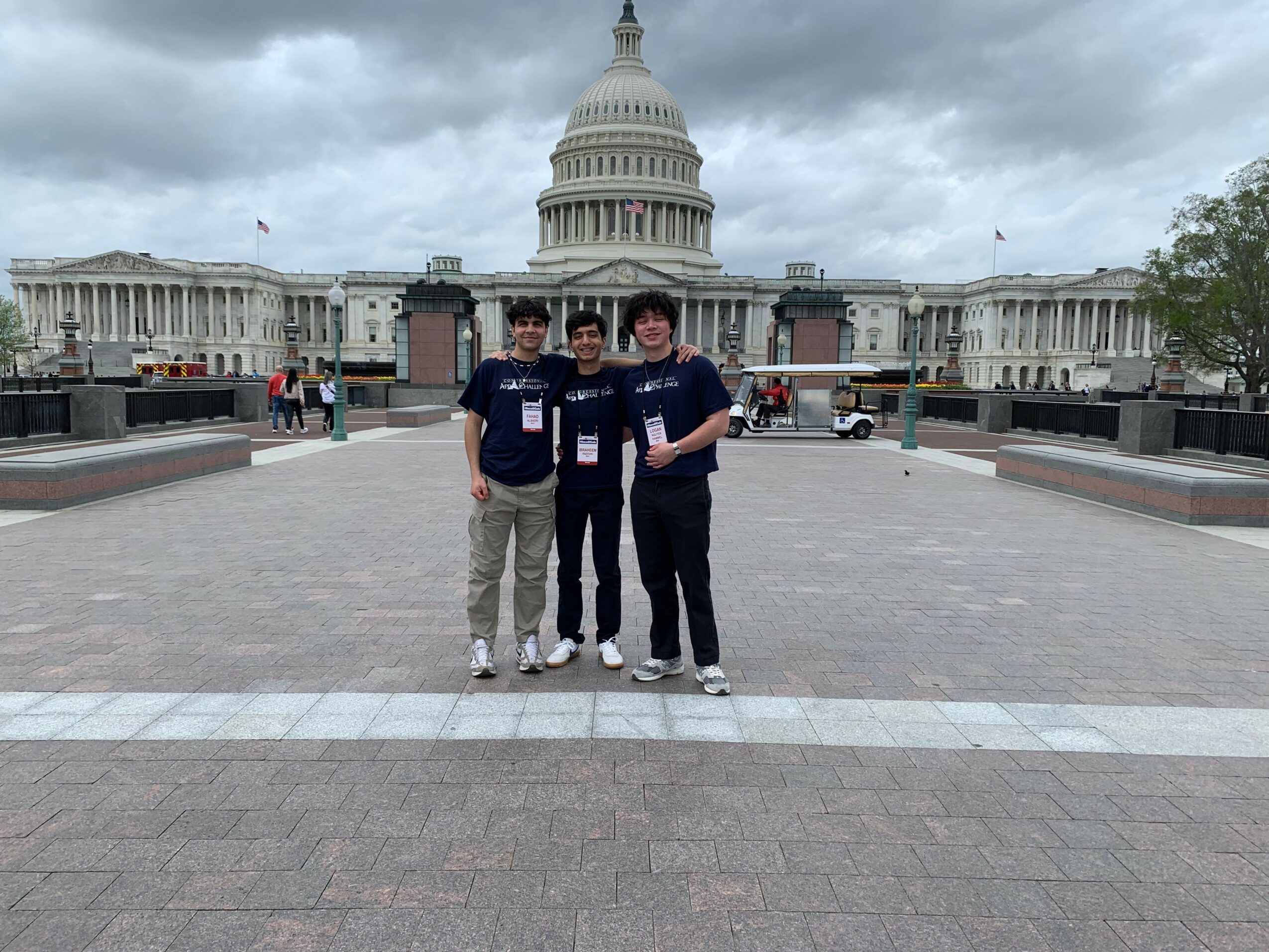 Three people stand in front of the U.S. Capitol building under cloudy sky, posing for a photo.