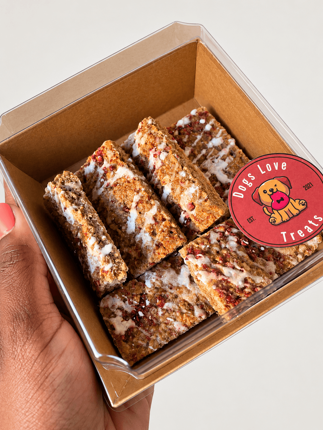 Box of assorted snack bars with a sticker reading 'Does Love Treats' featuring a dog illustration, held by a hand.