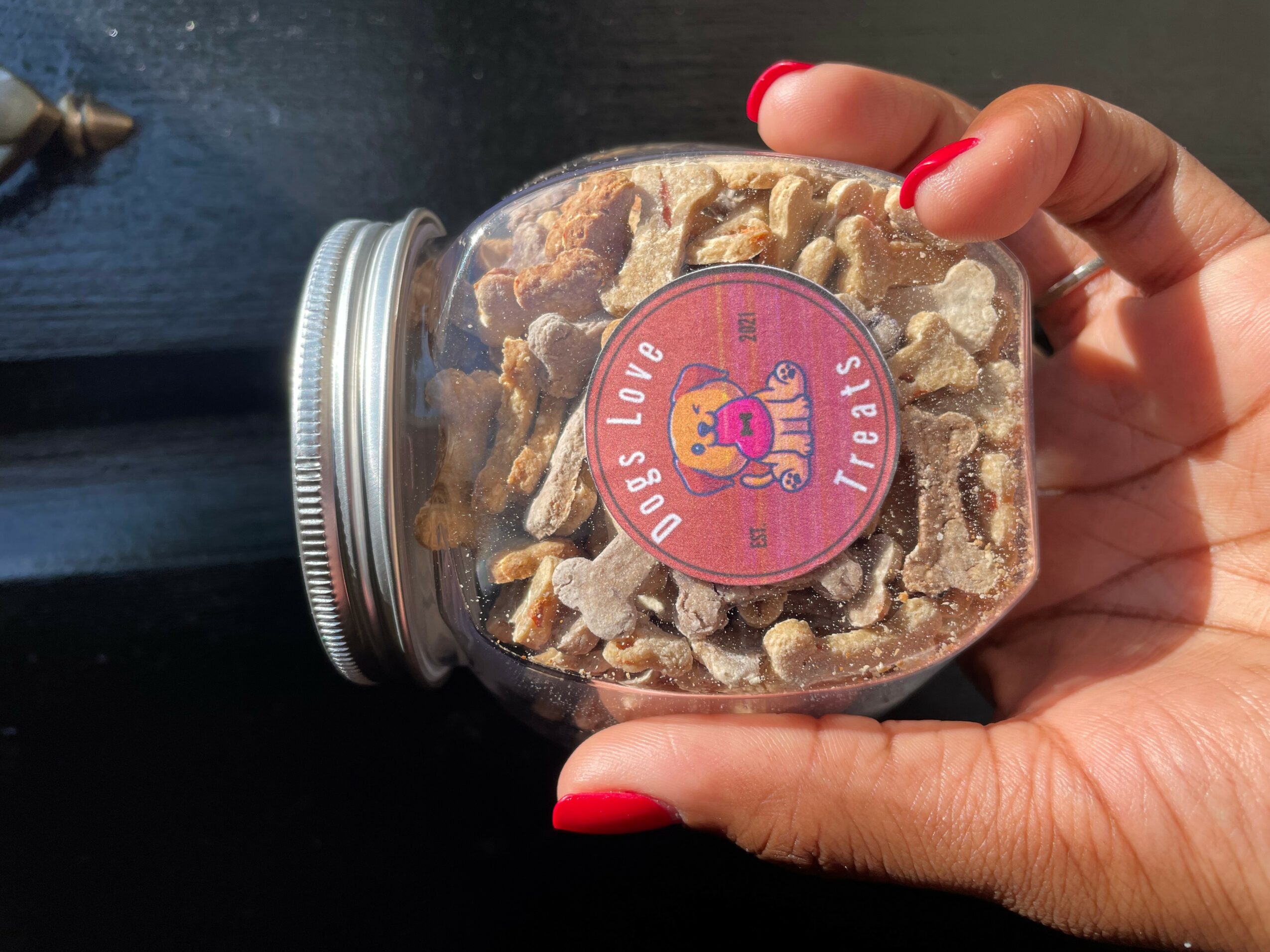 Hand holding a jar of cookies with a pink label featuring a cartoon character, against a dark background.