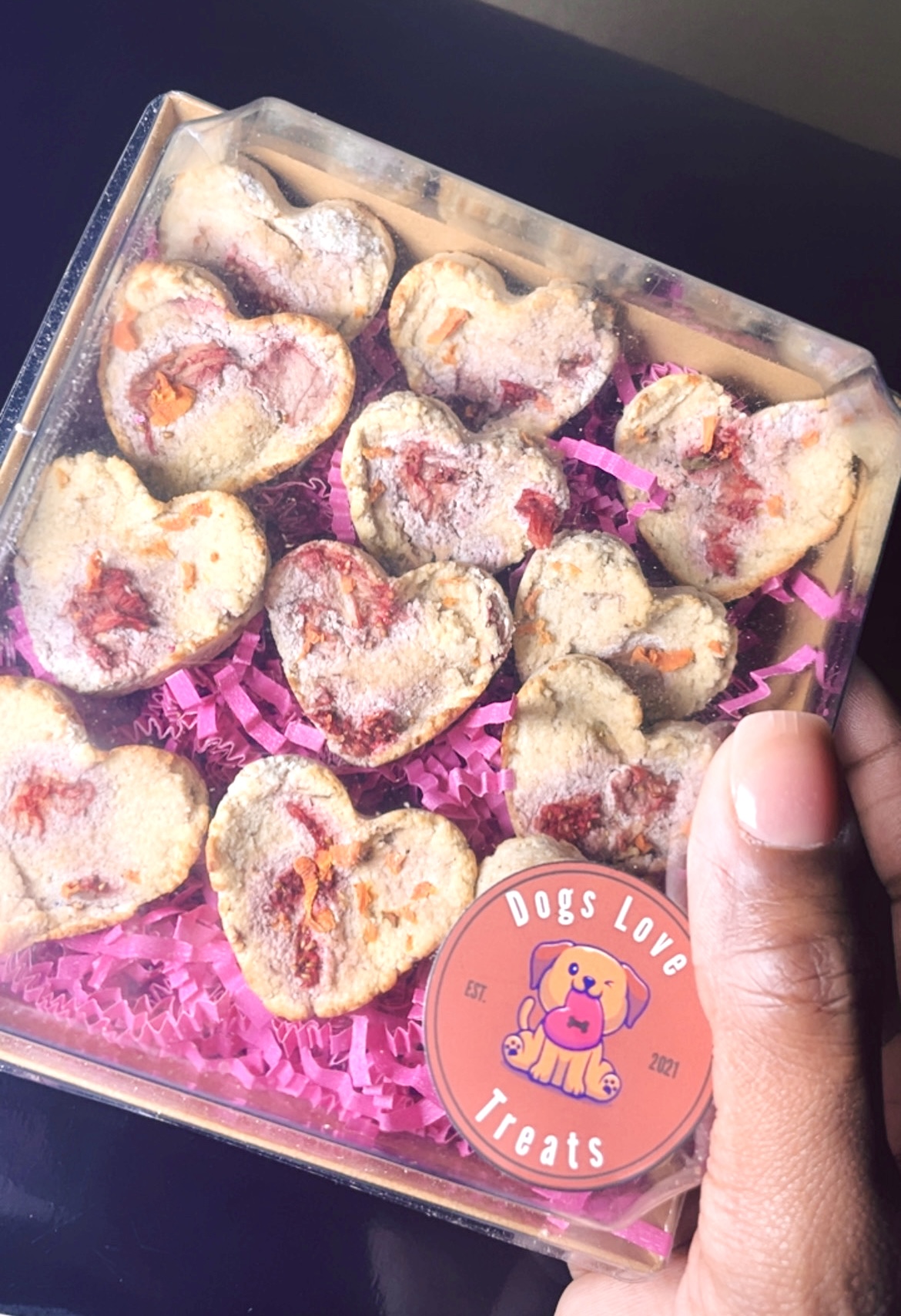 Clear box with heart-shaped dog treats on pink shredded paper, sticker with a dog and text 'Dogs Love Treats'.