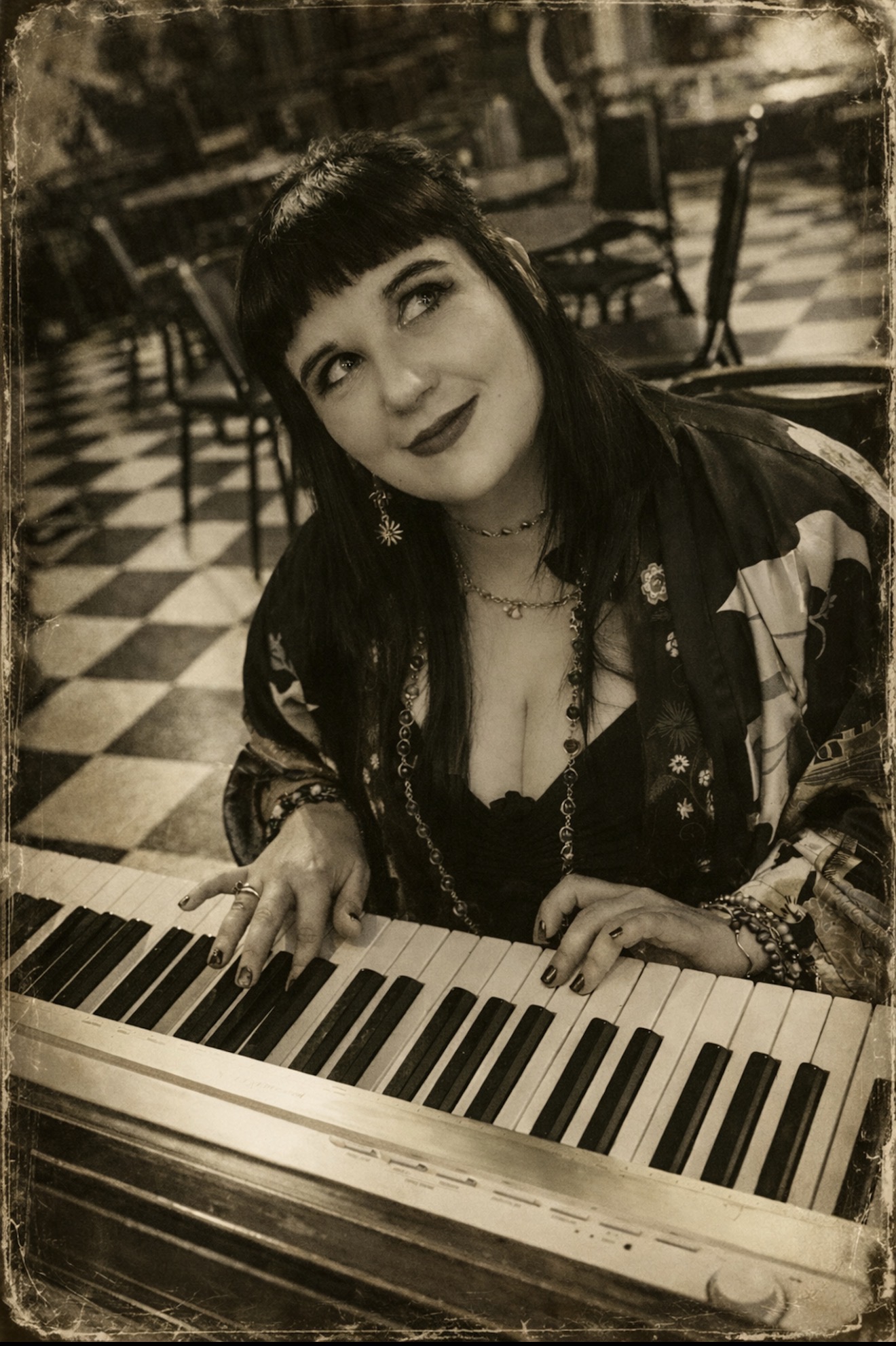 Woman with dark hair and bangs playing piano, looking upward, in a checkered floor setting.