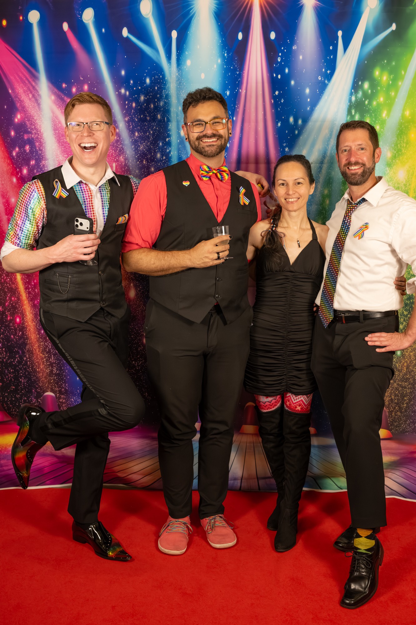 Four people in formal attire pose on a red carpet with colorful stage lights and a starry background.