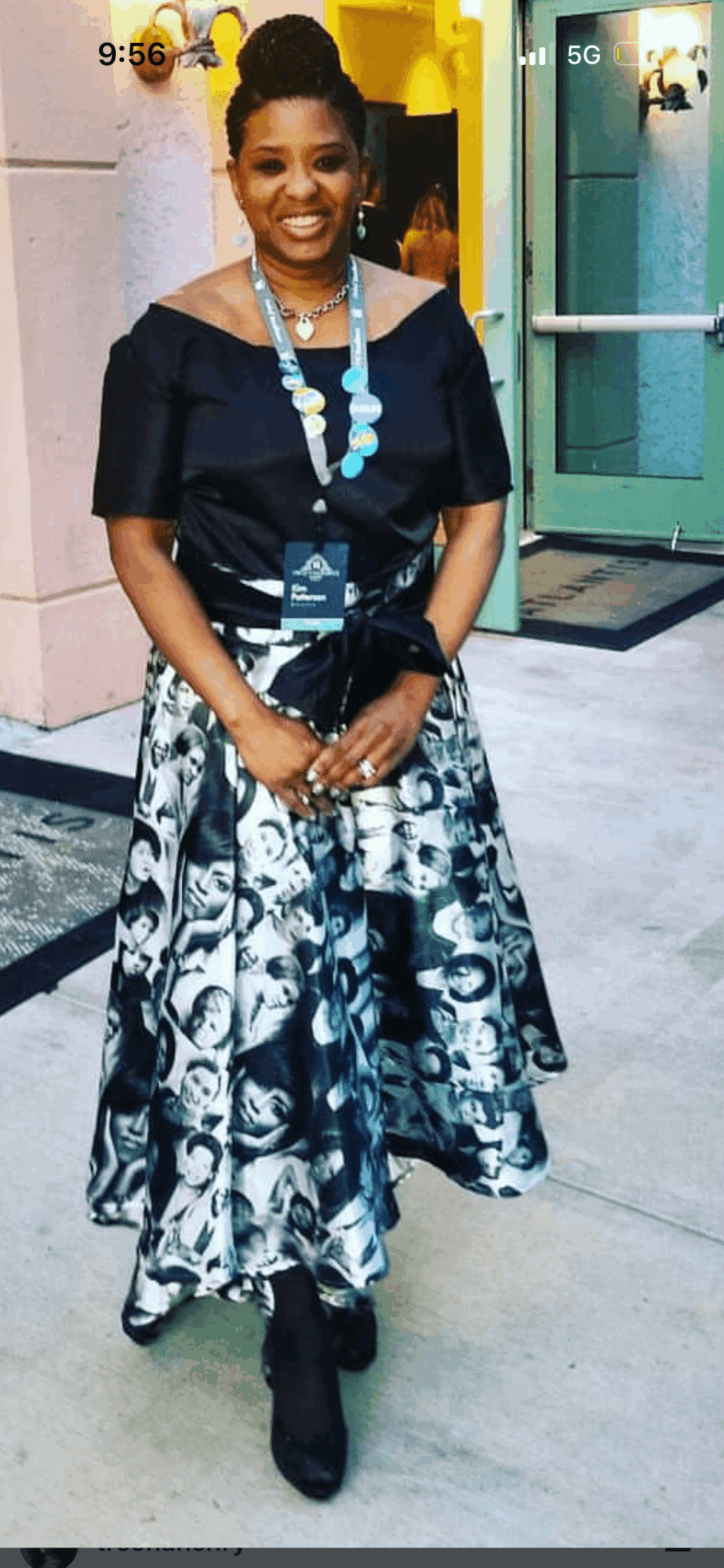 Woman in black and white patterned dress with jewelry, standing outside near a building entrance.