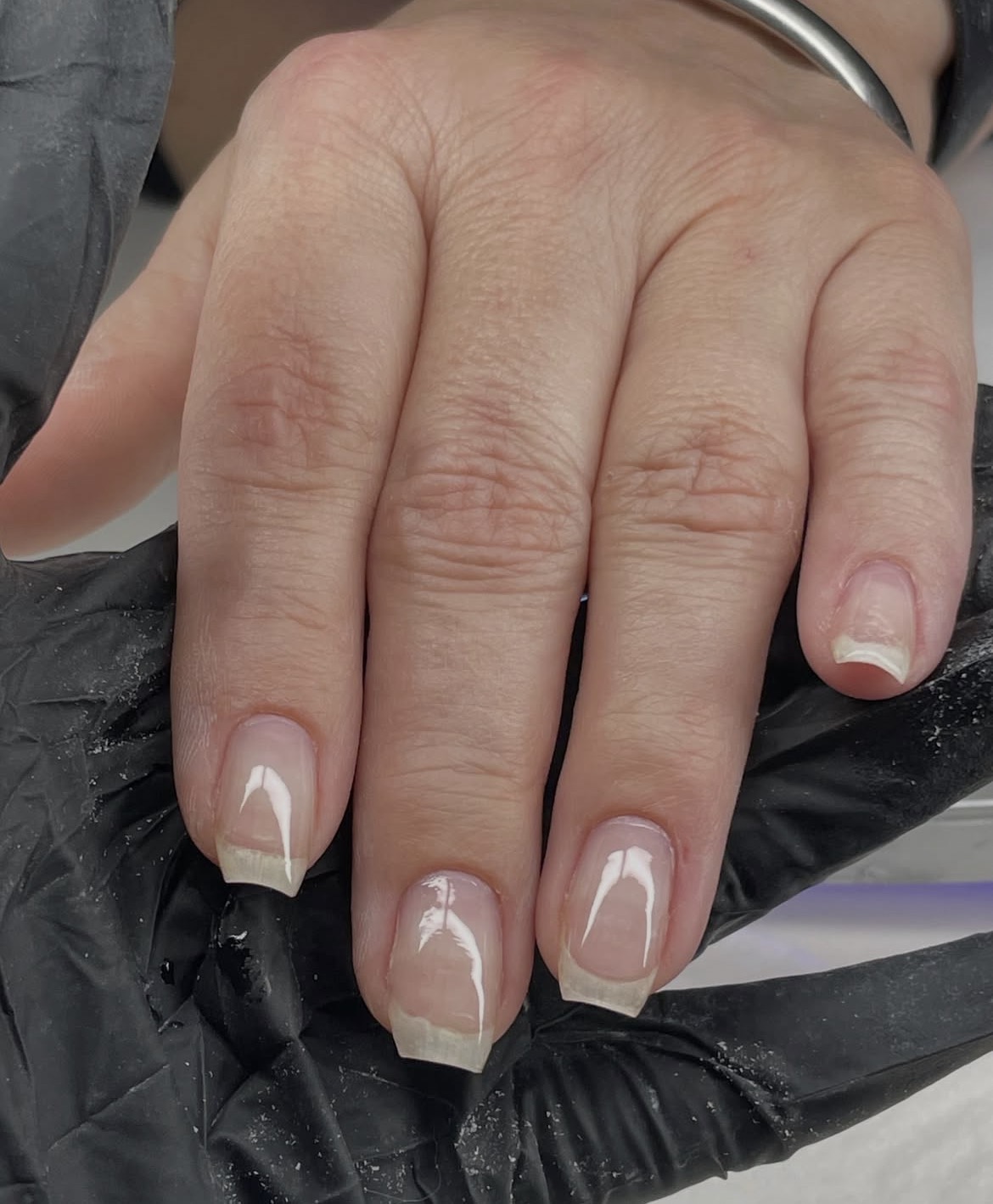 Close-up of a hand with neatly manicured nails, natural skin, and visible knuckles, resting on a black surface.