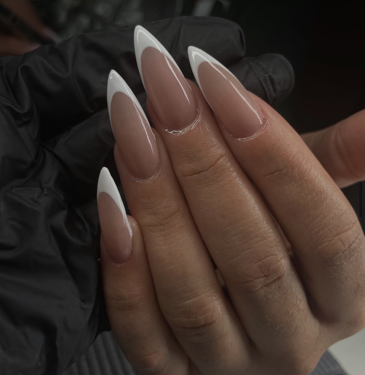 Close-up of a hand with long, almond-shaped nails painted with French manicure, held against a dark background.
