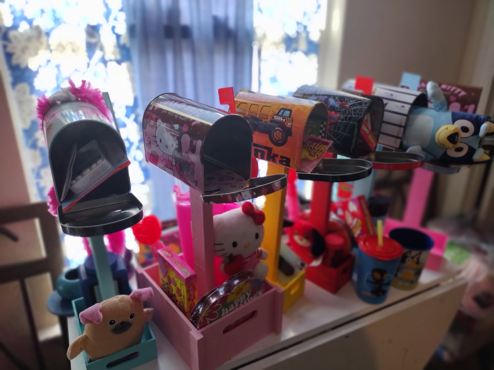 Collection of colorful toy cans and containers on a white surface, with a pink holder and a window in the background.