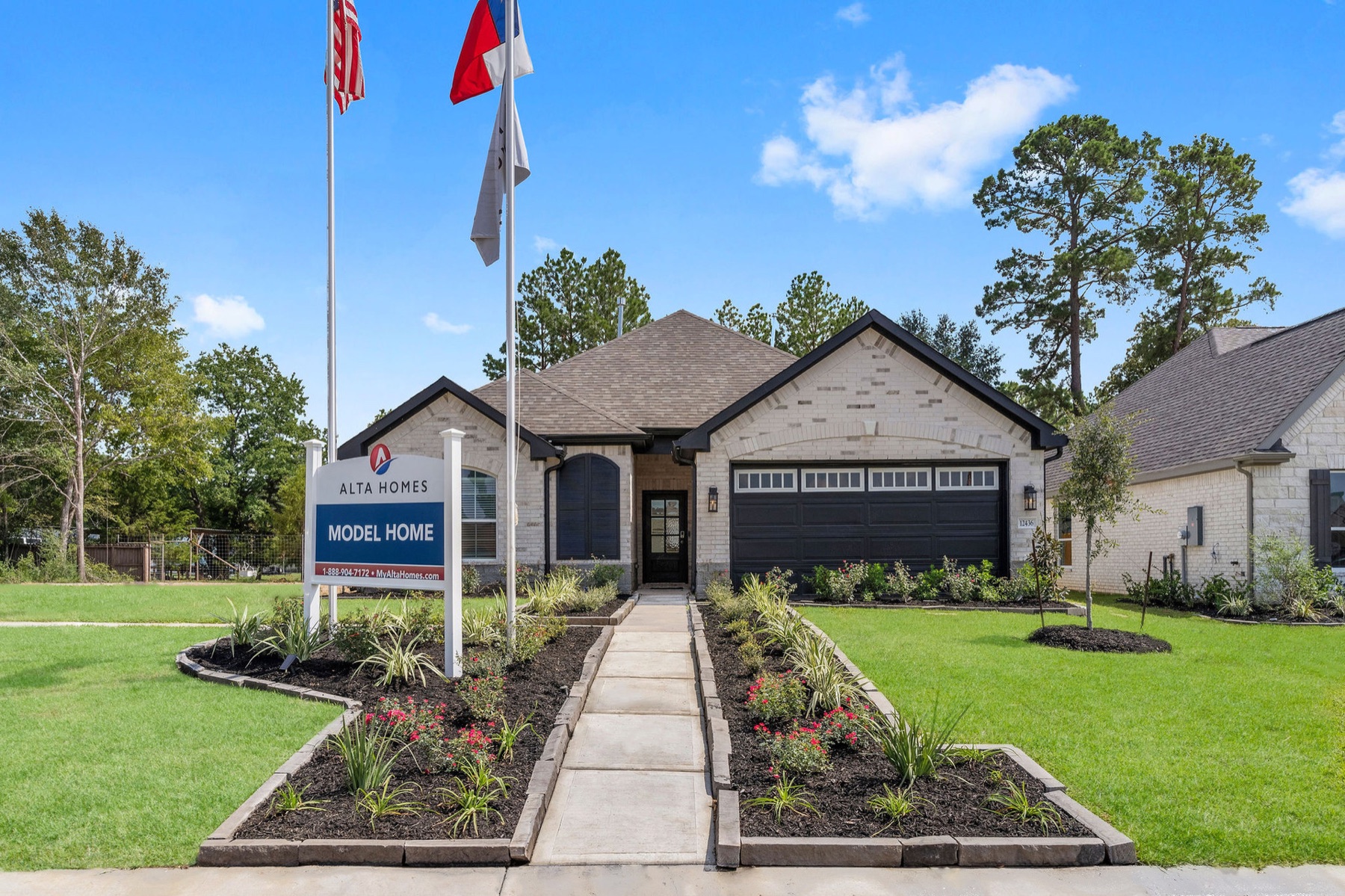 Front view of a house with a walkway, flags, and a sign, under a blue sky with trees in the background.
