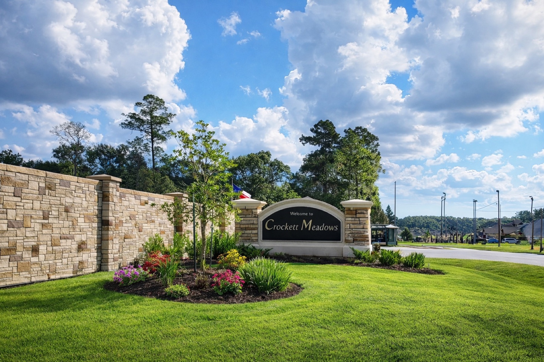 Entrance sign for Crescent Meadows with a stone wall, green lawn, and flowering plants, under a partly cloudy sky.