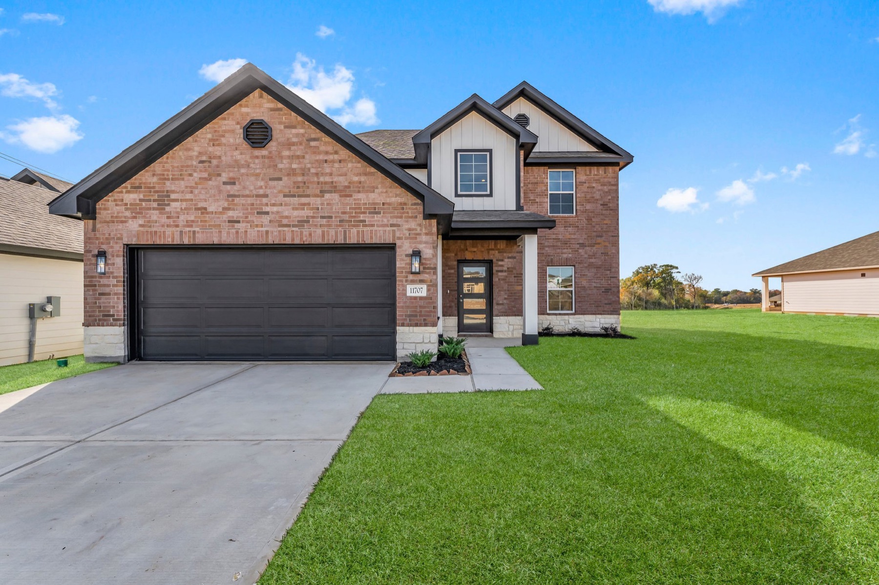 Two-story brick house with a black garage door, front door, and a well-maintained lawn under a blue sky.